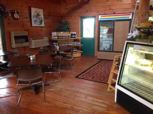 Cozy wooden interior of a café with tables, shelves of wine, and a display fridge. Green door and colorful decor visible.