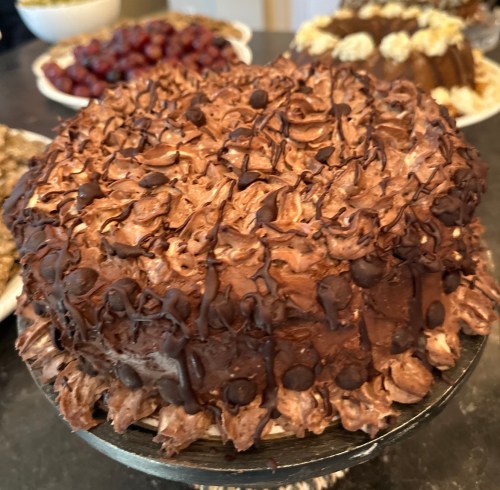 A chocolate cake with swirls of frosting and chocolate chips on top, displayed on a black cake stand.