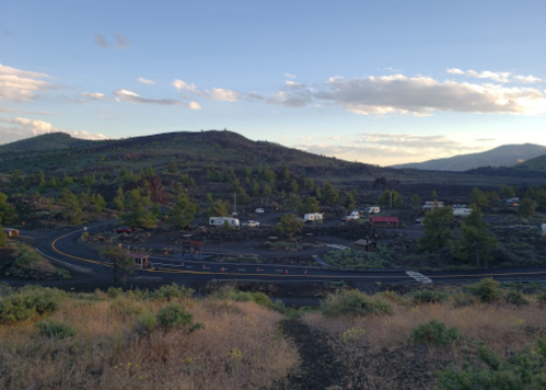 A scenic view of a winding road through a volcanic landscape with RVs and mountains in the background.