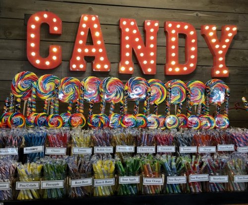 Colorful lollipops and candy displayed under a bright "CANDY" sign with lights, showcasing various flavors.