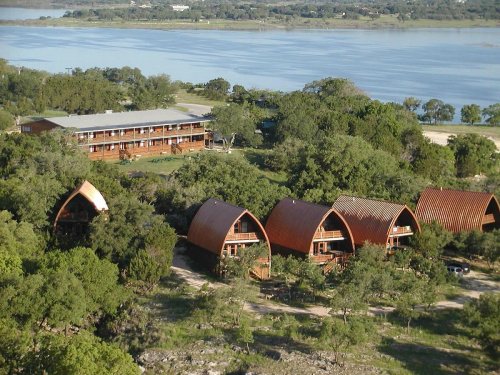 Aerial view of a lakeside resort featuring modern cabins and a larger building surrounded by trees.