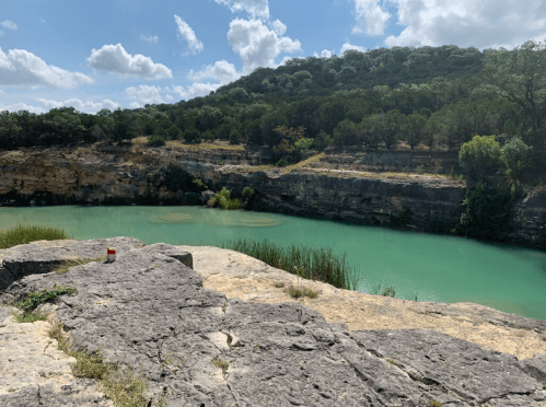 A serene landscape featuring a turquoise river surrounded by rocky cliffs and lush greenery under a partly cloudy sky.