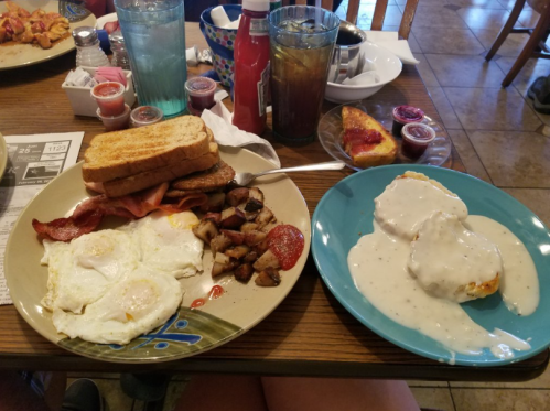 A hearty breakfast spread with eggs, toast, bacon, sausage, potatoes, and biscuits with gravy on a table.