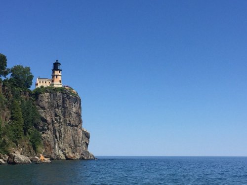 A lighthouse perched on a rocky cliff overlooking a calm blue sea under a clear sky.