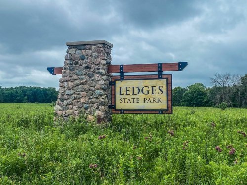 Sign for Ledges State Park, featuring a stone base and surrounded by a green field under a cloudy sky.
