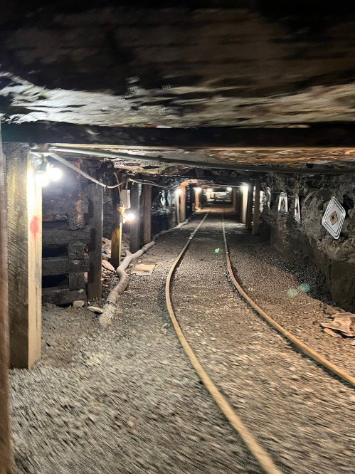 A dimly lit underground mine tunnel with wooden supports and railway tracks running through it.