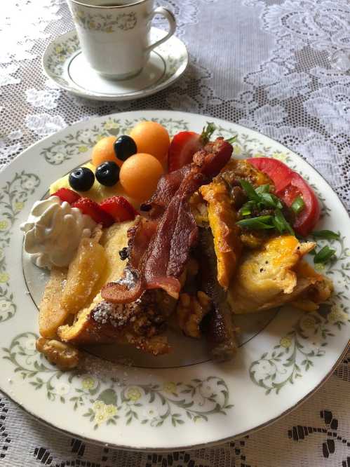 A plate of breakfast featuring bacon, eggs, fruit, and a dollop of cream, with a cup of coffee in the background.