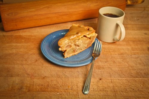 A slice of pie on a blue plate next to a mug of coffee, set on a wooden countertop.