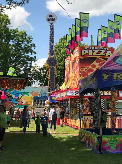 A vibrant fair scene with colorful rides, food stalls, and people enjoying the festivities on a sunny day.