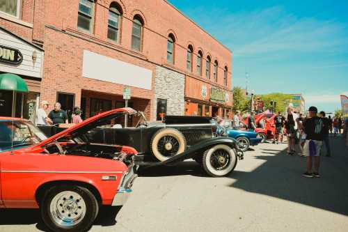 A street scene featuring classic cars on display, with people admiring them and historic buildings in the background.