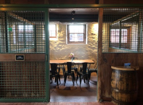 A rustic dining area with a wooden table, metal chairs, and a flower vase, enclosed by metal grates and wooden walls.