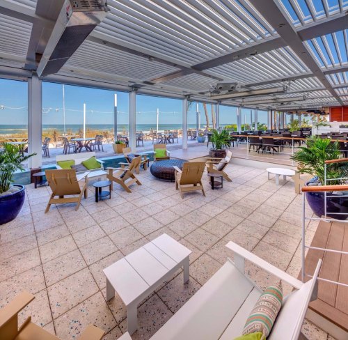 A modern beachfront patio with seating, plants, and a view of the ocean, featuring a bright and inviting atmosphere.
