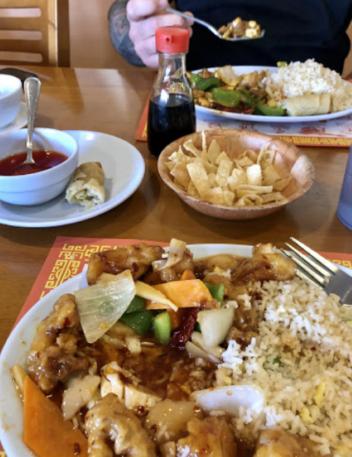 A table set with two plates of Chinese food, soy sauce, a bowl of dipping sauce, and a side of crispy chips.