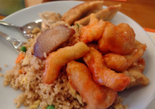 A plate of fried rice topped with sweet and sour chicken, pork, and dumplings.