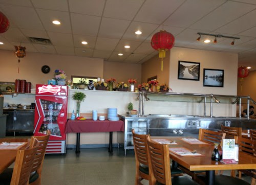 Interior of a restaurant featuring red lanterns, a buffet area, and a drink cooler, with tables and decorative plants.