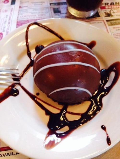 A chocolate dessert ball drizzled with chocolate sauce on a white plate, with a fork beside it.