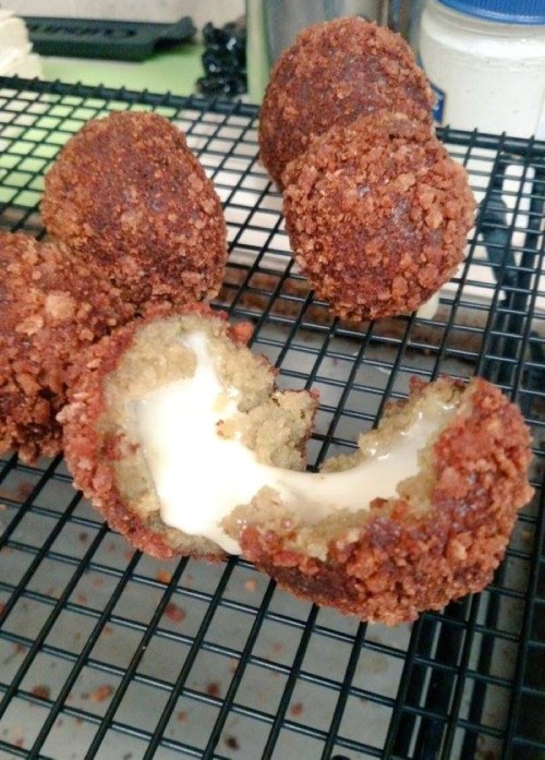 Golden-brown fried balls on a cooling rack, with one cut open to reveal gooey melted cheese inside.