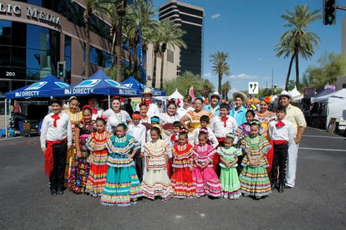 A vibrant group of children and adults in traditional Mexican attire poses together at a festive outdoor event.