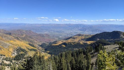 A panoramic view of a mountainous landscape with autumn foliage, valleys, and a clear blue sky.
