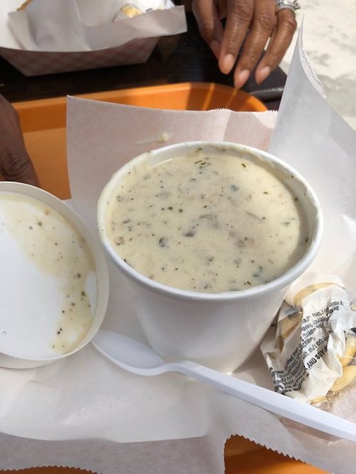A cup of creamy soup with herbs, accompanied by a small container and a spoon, on a tray with a napkin.