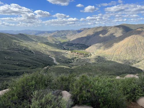 A panoramic view of rolling green hills and valleys under a partly cloudy sky.