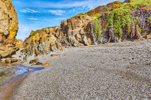 A rocky beach with colorful cliffs and scattered pebbles under a clear blue sky.