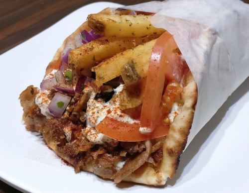 A wrapped sandwich filled with meat, fries, tomatoes, onions, and sauce, served on a plate.