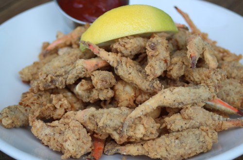 A plate of crispy fried soft-shell crabs garnished with a lemon wedge and served with a side of dipping sauce.