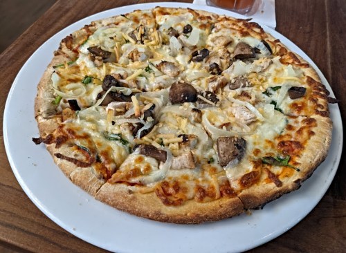 A freshly baked pizza topped with cheese, mushrooms, onions, and herbs on a wooden table.