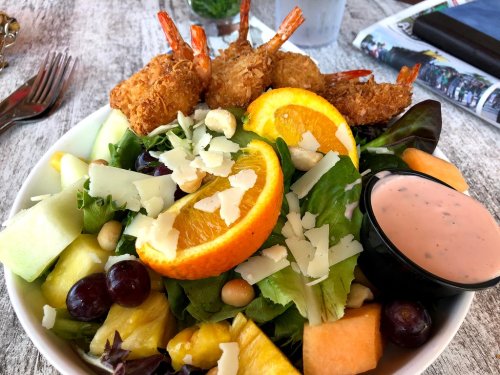 A colorful salad with shrimp, mixed greens, fruits, and a creamy dressing on the side, served in a bowl.