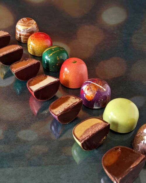 A colorful assortment of chocolate truffles, some whole and some cut in half, showcasing their creamy fillings.