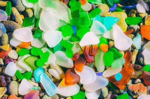Colorful sea glass pieces in various shapes and sizes scattered among smooth pebbles on a beach.