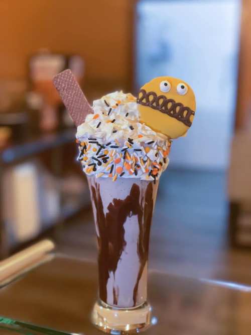 A tall milkshake topped with whipped cream, sprinkles, a wafer, and a cookie with a smiling face.