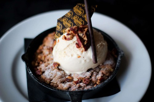 A warm dessert in a cast-iron skillet topped with ice cream, nuts, and a decorative chocolate piece.