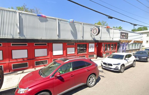 A red building with a corrugated metal roof, featuring large windows and parked cars in front.