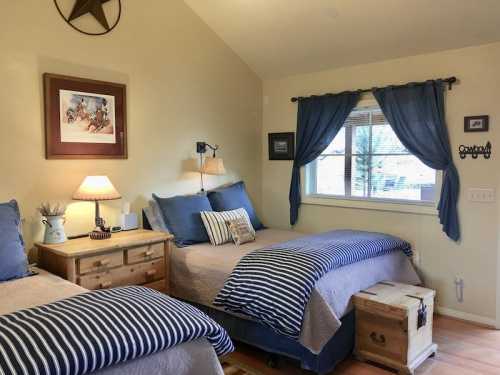 Cozy bedroom with two beds, blue striped bedding, wooden furniture, and a window with blue curtains.