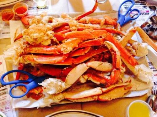A large platter of crab legs with blue scissors for cracking, served on a table with dipping sauces.