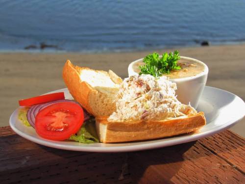 A plate with a sandwich filled with shredded chicken, served with a side of soup, lettuce, tomato, and onion.
