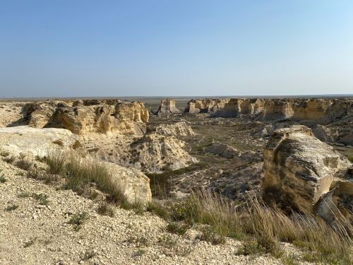 A vast canyon landscape with layered rock formations and sparse vegetation under a clear blue sky.