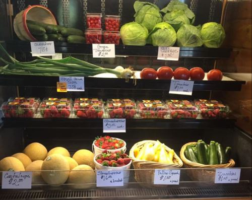 A display of fresh vegetables and fruits, including cucumbers, tomatoes, melons, and strawberries, with price tags.