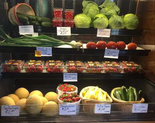 A display of fresh vegetables and fruits, including cucumbers, tomatoes, melons, and strawberries, with price tags.