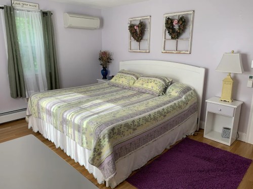 A cozy bedroom featuring a large bed with a patterned blanket, two wall decorations, and a lamp beside a nightstand.