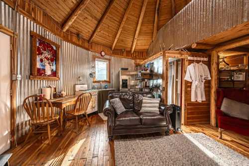 Cozy interior of a round cabin featuring wooden beams, a leather sofa, dining area, and rustic decor.