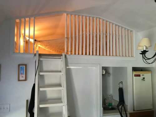 A cozy loft space with a white railing, accessed by a ladder, illuminated by warm light.