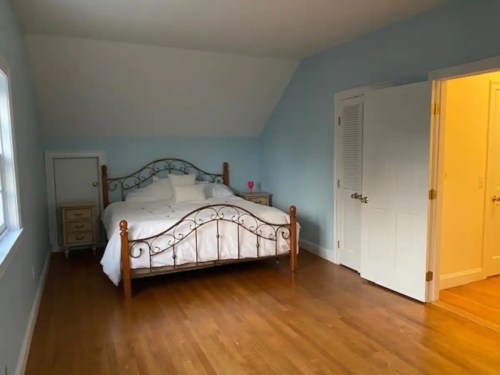 A cozy bedroom with a metal bed frame, light blue walls, hardwood floors, and a closet door.