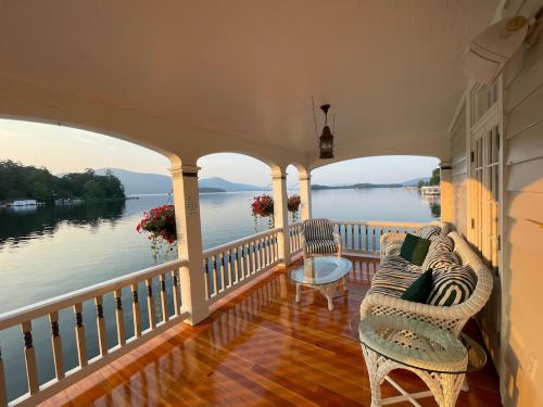A serene porch overlooking a calm lake, featuring a wicker sofa and potted flowers, with mountains in the background.