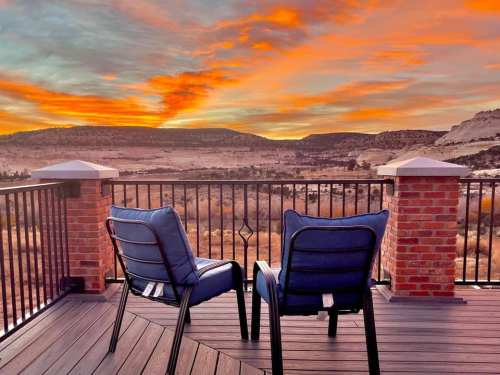Two blue chairs on a deck overlooking a scenic sunset with vibrant orange and pink hues in the sky.