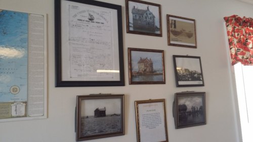 A wall displaying framed historical documents and photographs, including a map and various buildings.
