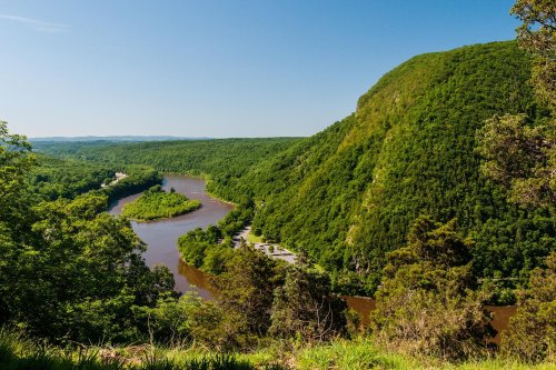A scenic view of a winding river surrounded by lush green hills under a clear blue sky.