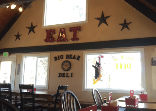 Interior of a deli with a "EAT" sign, stars on the wall, and large windows. Tables and chairs are arranged for dining.